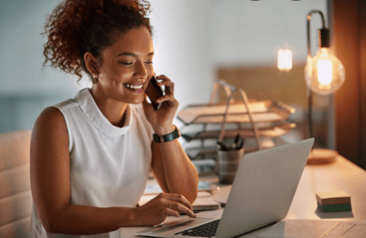 A woman at home speaking on her cell phone and looking at her laptop.