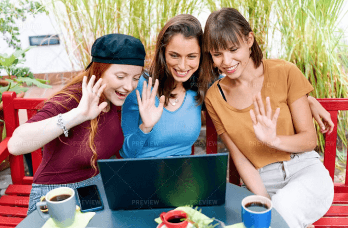 Three women waving to someone communicating via laptop.