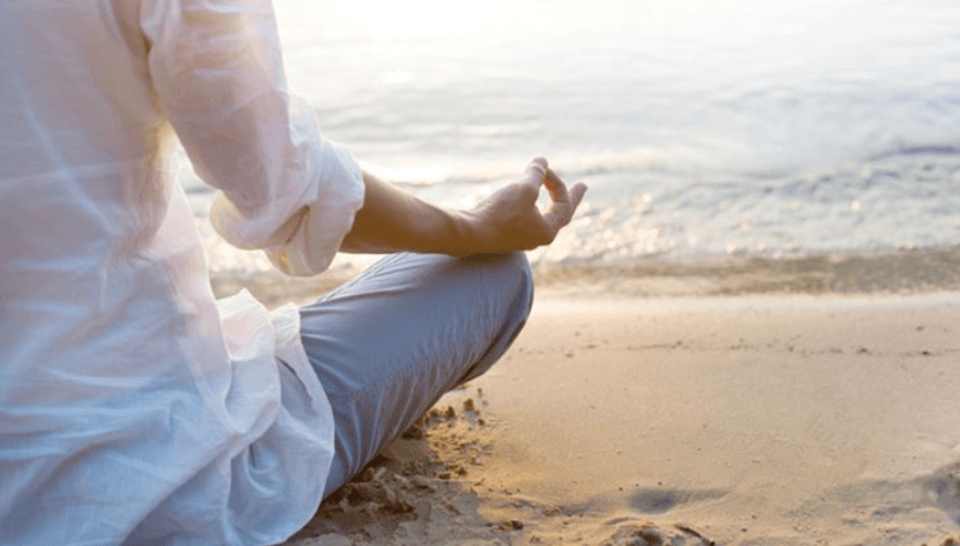 A woman mediating on the beach in front of the ocean.