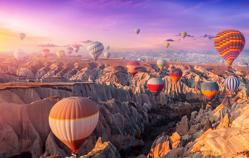 Aerial view amazing sunrise landscape in Cappadocia with colorful hot air balloon fly in sky over deep canyons, valleys. Concept banner travel Turkey.