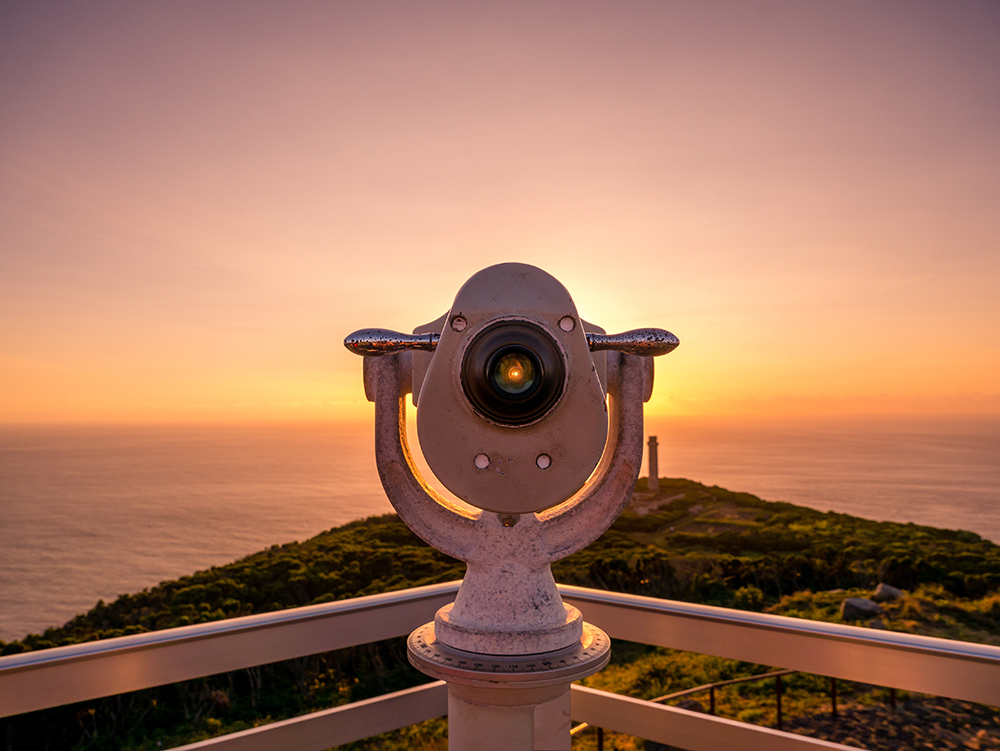Image of viewpoint with binoculars during colorful sunset pointing at the ocean