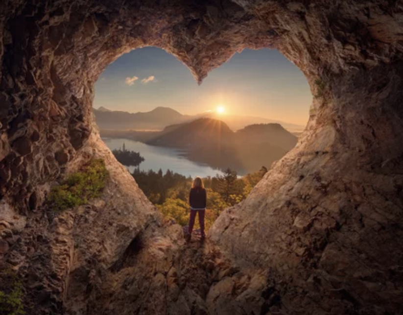 Woman standing in a heart shaped tunnel looking out into a mountain landscape