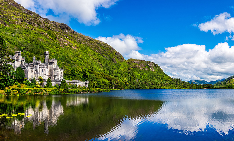 An Irish castle on the bank of a lake with the sky reflecting in the water.