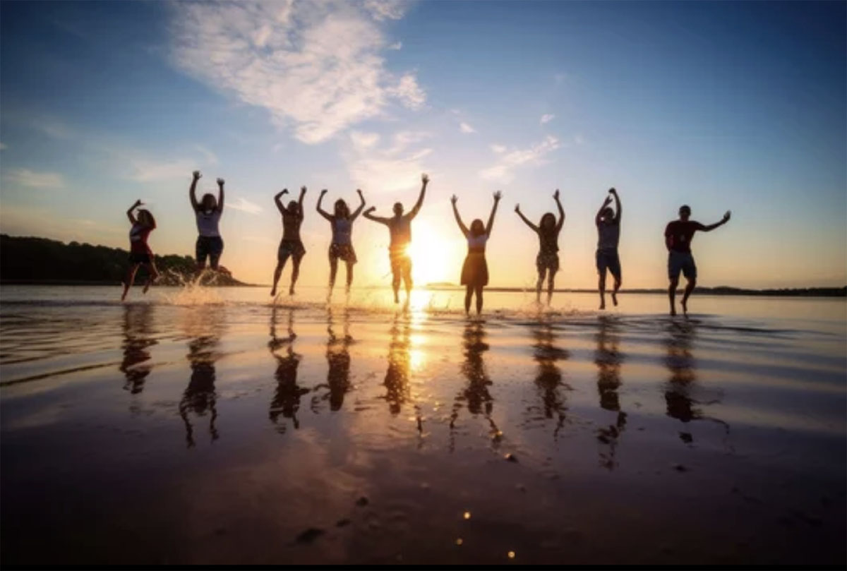 People jumping for joy on a beach at sunset